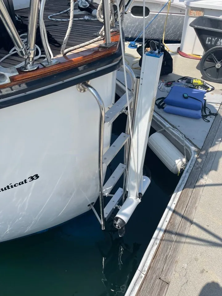 A DockStar on the stern of a Nauticat 33 at a dock, the leg running down past the boarding ladder with the propeller a foot or so under the surface, close to the dock edge and a fender.