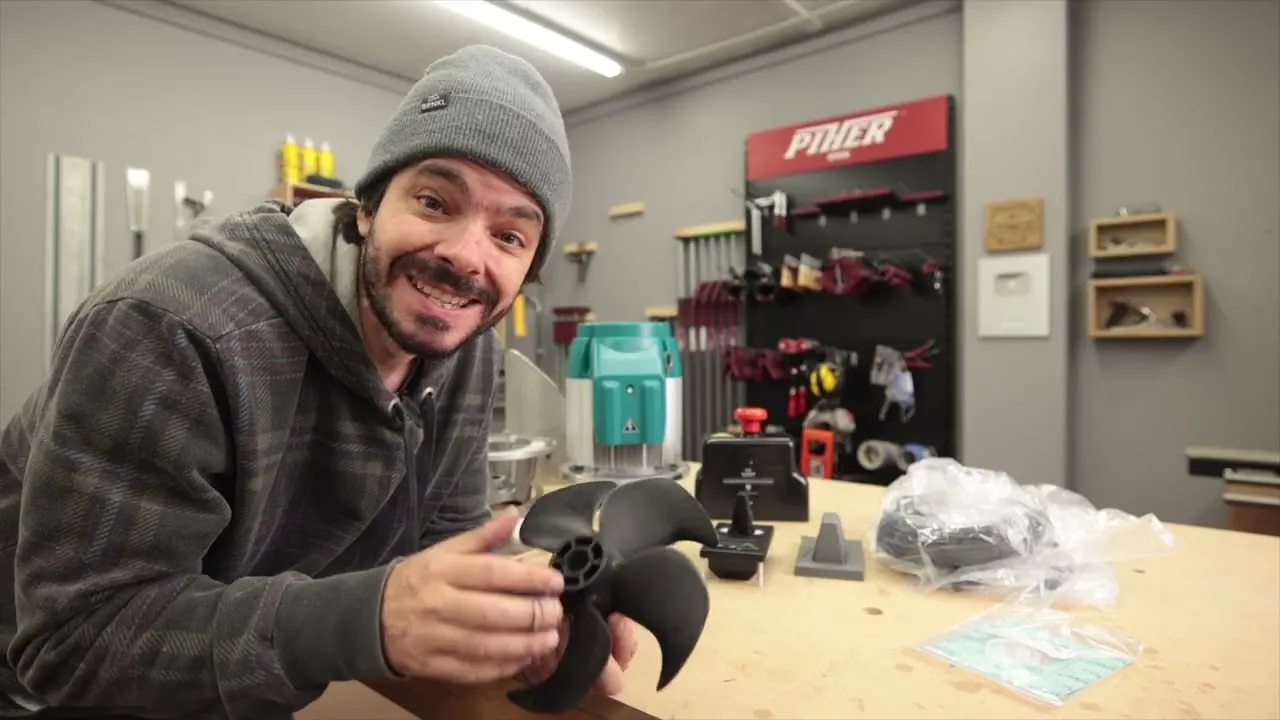 A still from Sleipner's E150 video: a man in a knit cap at a workbench holding the thruster's black propeller, the motor and controller behind him.